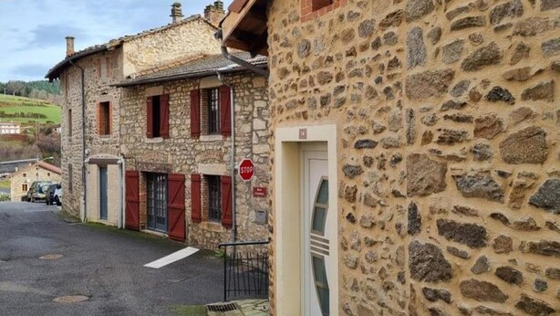 Un bâtiment en pierre avec une porte rouge et un panneau de signalisation indiquant l’obligation de s’arrêter.