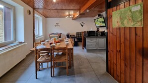 L’intérieur chaleureux d’un chalet comprend une table à manger en bois, des chaises, un coin cuisine et un téléviseur.