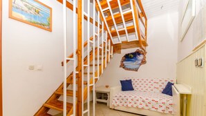 Una escalera con barandillas de madera lleva a un dormitorio con una cama blanca y un cojín azul.