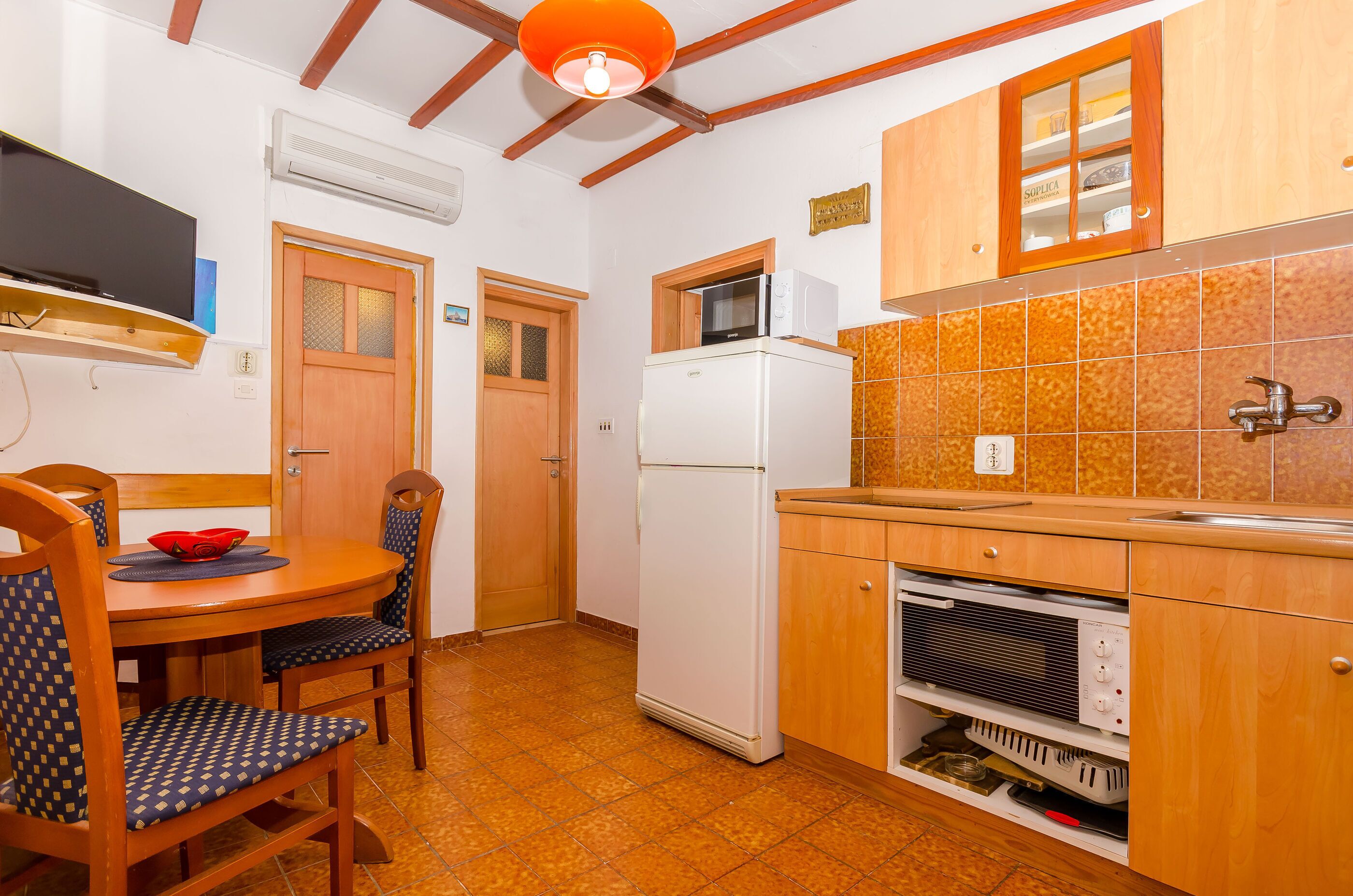 A compact kitchen with wooden cabinets, a white refrigerator, a microwave, and a dining area with a table and chairs.