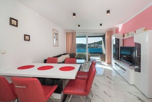 Ein modernes Wohnzimmer mit Essbereich, Fernseher und Meerblick.