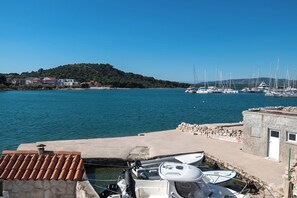A marina with boats docked, a stone wall, and a small building with a door. - Apartments Villa Summertime (Tisno)