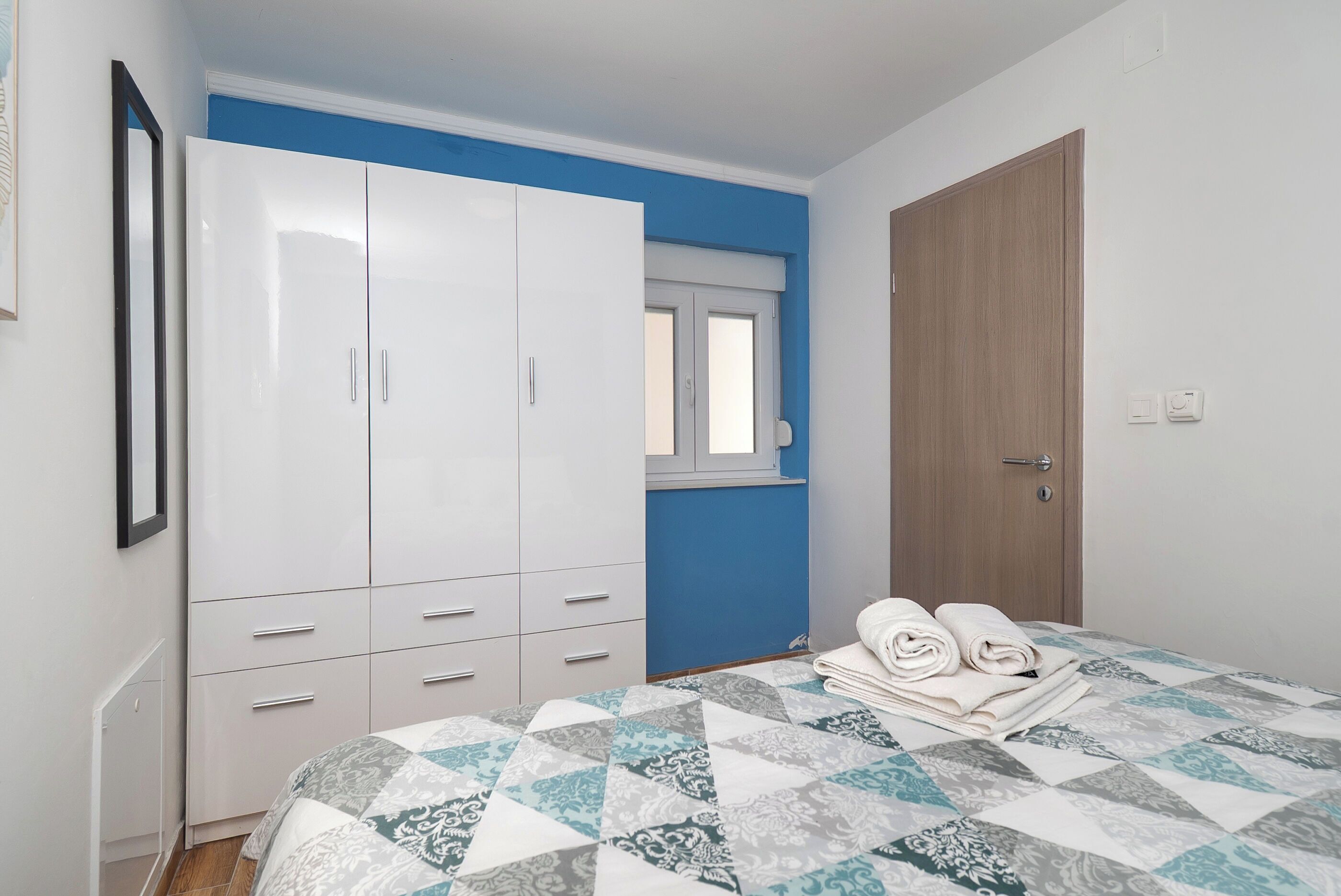 A bedroom with a bed, a wardrobe, a window, and a door.