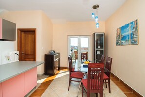 A compact kitchen with a dining area, a wooden door, and a view through a glass door. - Apartment Villa Zlatna (Tisno)