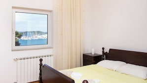 A bedroom with a bed, a nightstand, a window with a view of boats and a marina. - Apartment Villa Zlatna (Tisno)