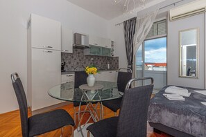 A modern kitchen with white cabinets, a glass dining table, and a vase with flowers. - Apartment Tea (Crikvenica)