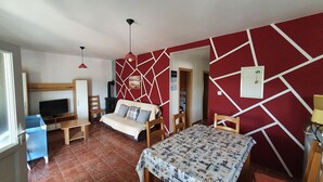 A bedroom with a bed, a desk, a chair, a TV, a red wall with white geometric patterns, and a fireplace. - Apartments Marin (Lopar)