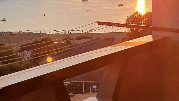 A sunset view from a window overlooking a calm body of water with boats and a pier. - Apartments Marin (Lopar)