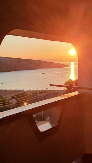 A sunset view from a window overlooking a calm body of water with boats and a pier. - Apartments Marin (Lopar)