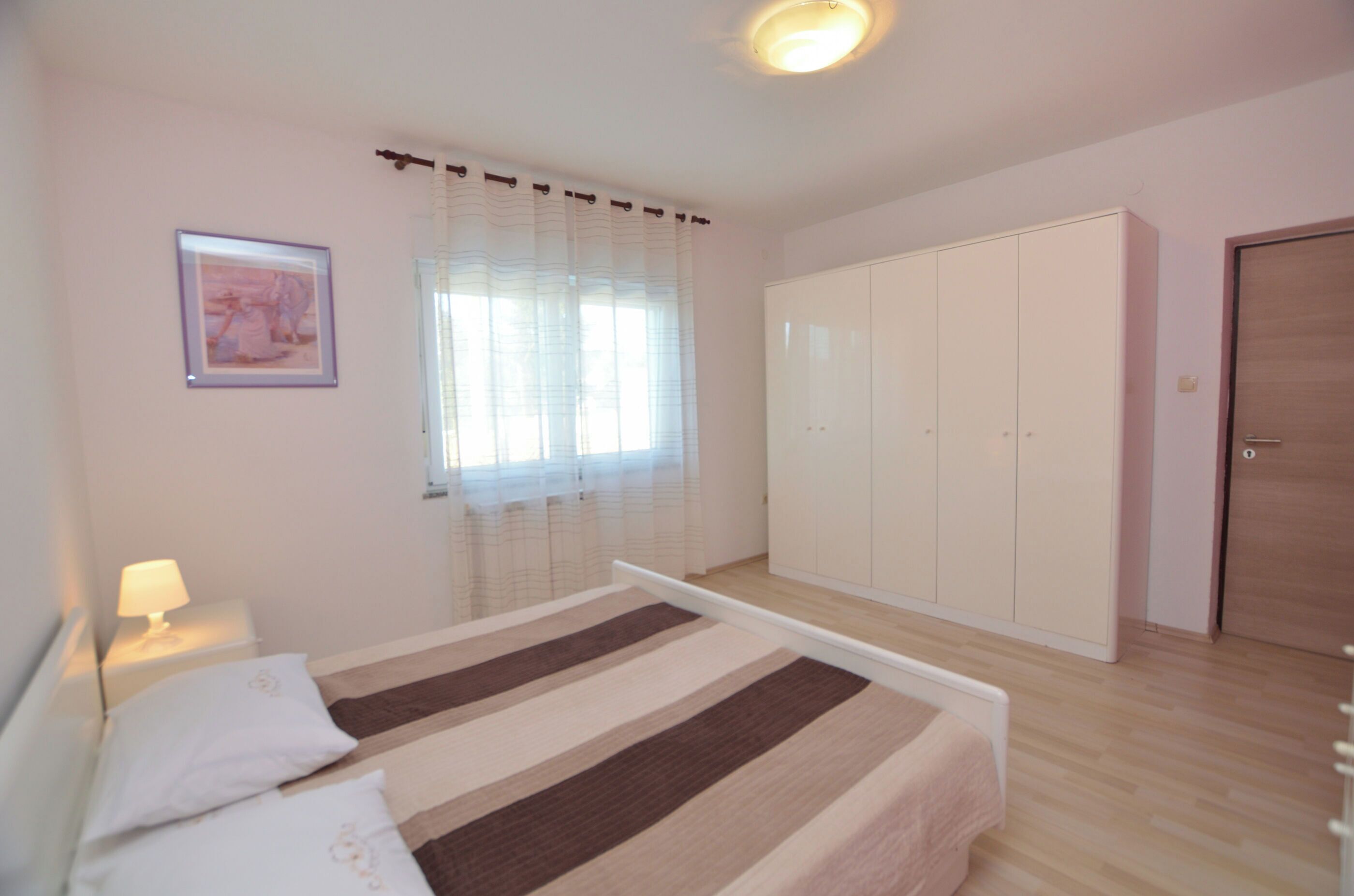 Een slaapkamer met een bed, een kledingkast, een nachtkastje en een raam met gordijnen.