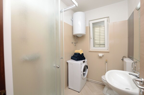 Une petite salle de bain équipée d’un lave-linge, de toilettes et d’un lavabo.