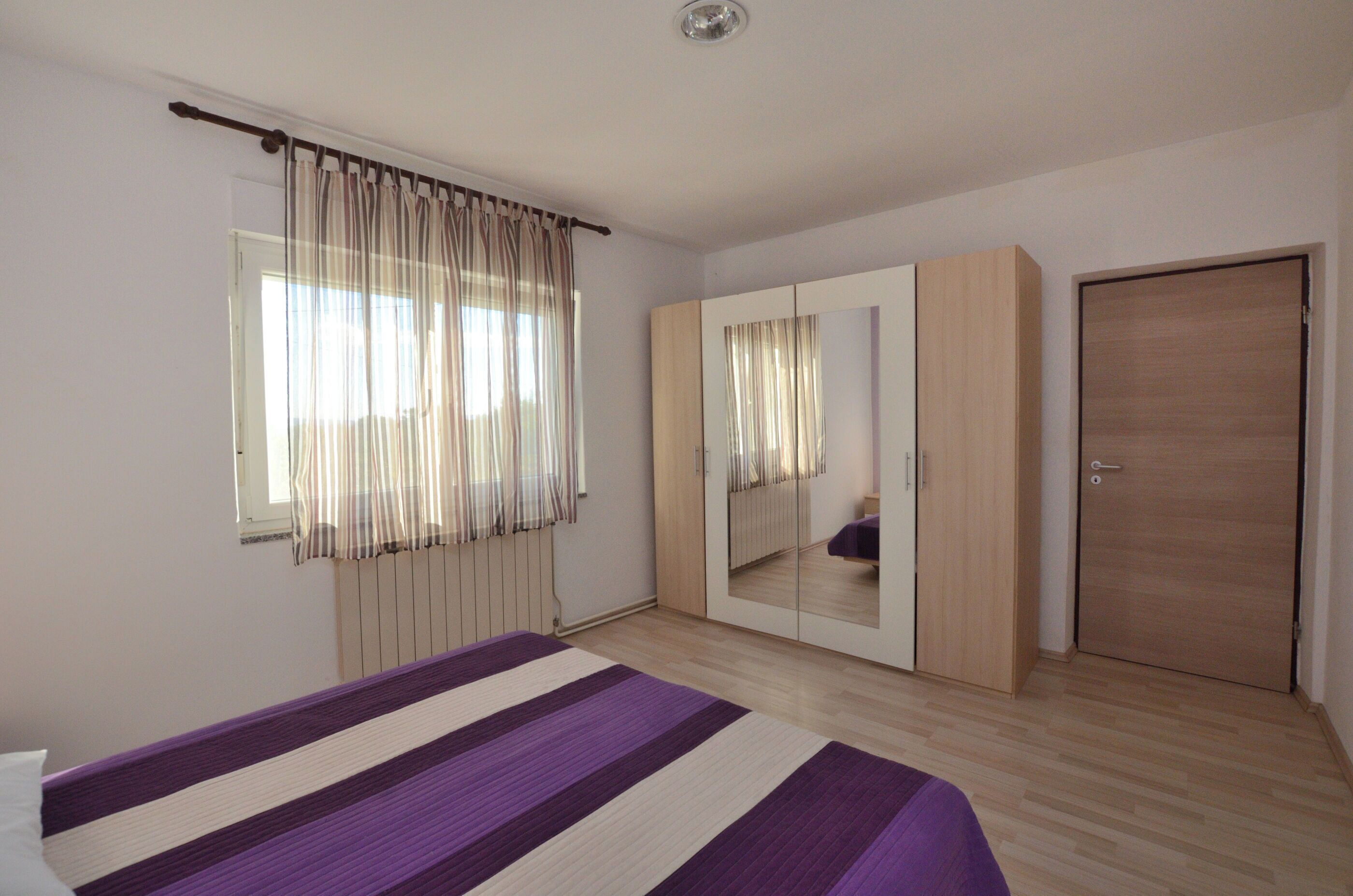 A bedroom with a bed, a wardrobe, a mirror, and a door.