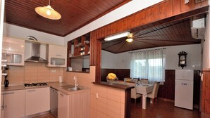 A kitchen with wooden cabinets, a sink, a stove, and a refrigerator. There is a dining table with chairs and a chandelier. - Villa Mirka (Barban)