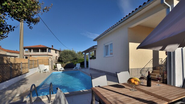 A poolside area with a wooden table, lounge chairs, and a clear blue pool. - Villa Mirka (Barban)