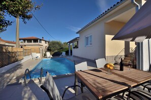 Un espace aménagé au bord de la piscine, avec une table en bois, des chaises longues et une piscine à l’eau d’un bleu limpide.
