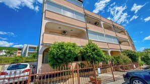 A multi-story building with balconies, a gated parking area, and a clear blue sky. - Apartment Brdar (Crikvenica)