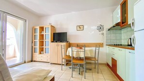 A compact kitchen with a dining table, a cabinet with glass doors, a television, and a kitchenette. - Apartment Brdar (Crikvenica)