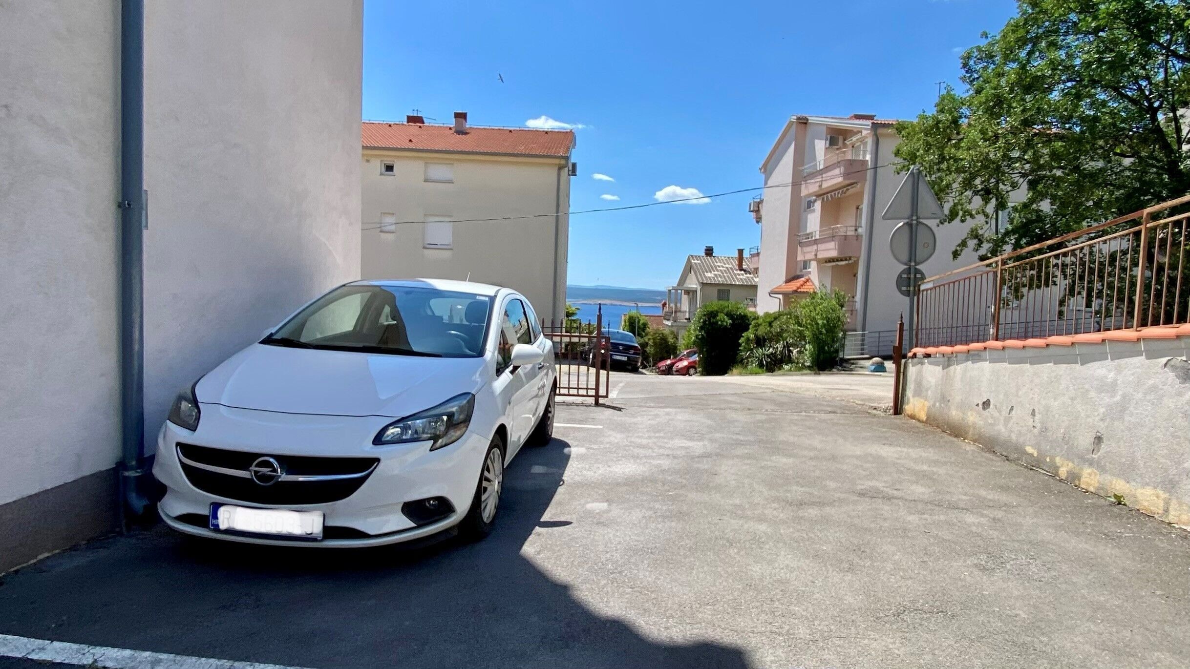 A white car parked in a narrow driveway with a clear view of the sea in the background.