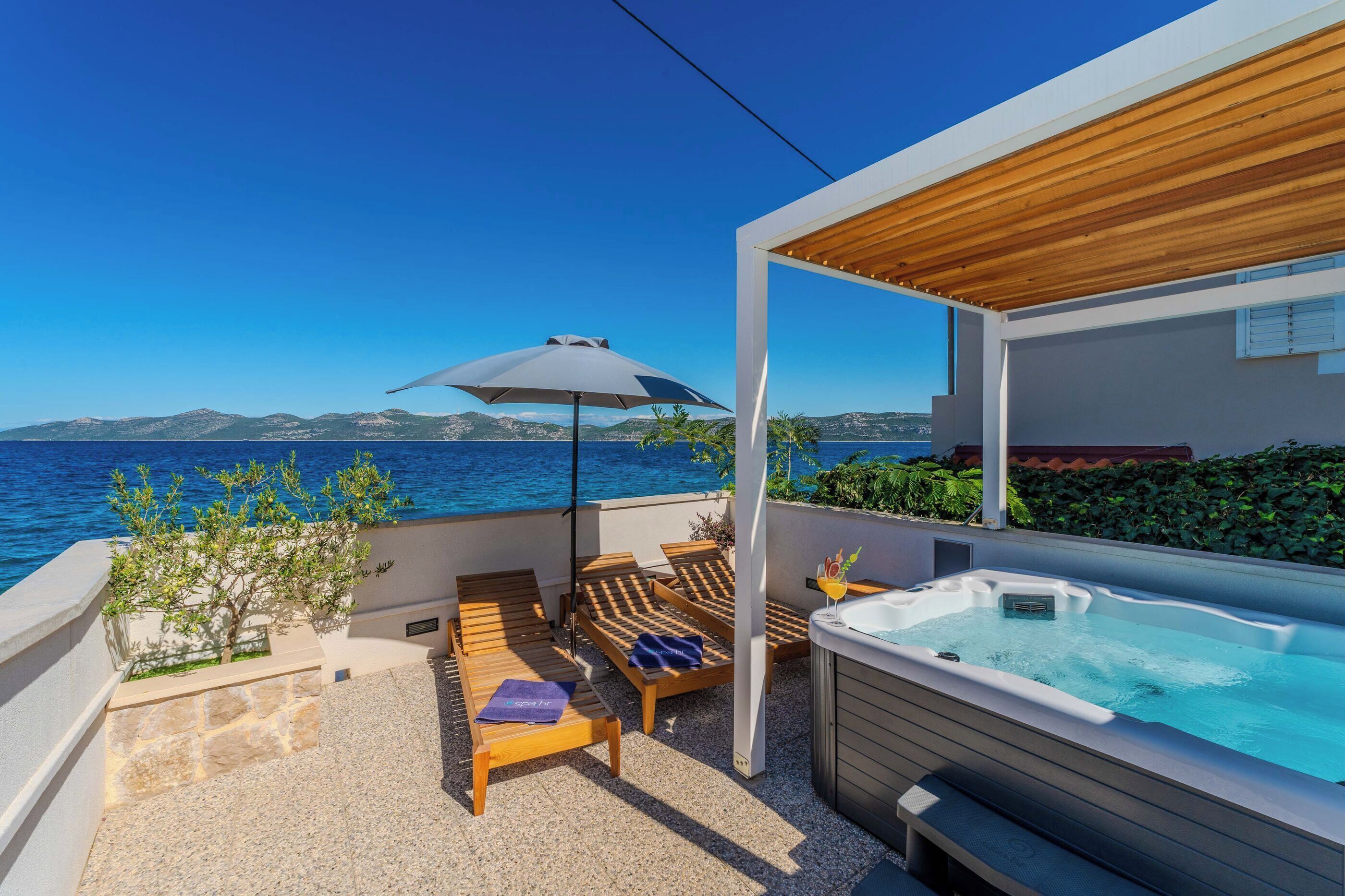 Una terraza moderna al aire libre con hidromasaje, sillones de descanso y vistas al mar.