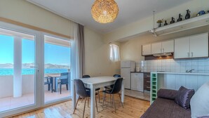 Eine moderne Küche mit weißen Schränken, ein Essbereich mit Tisch und Stühlen und ein großes Fenster mit Blick auf ein Gewässer.