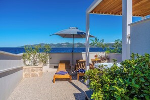A balcony with wooden lounge chairs, a table with a drink, and a view of the sea and mountains. - Apartment Iva (Zadar)