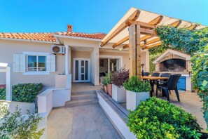 A house with a tiled roof, a wooden pergola, a barbecue area, and a garden with potted plants. - Apartment Iva (Zadar)
