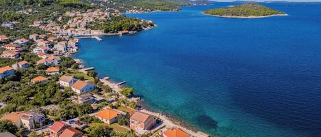An aerial view of a coastal town with houses along the shoreline, a clear blue sea, and a small island in the distance.