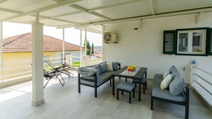 A covered outdoor seating area with a sofa, table, and chairs. - Apartments Pleasures (Jelsa)