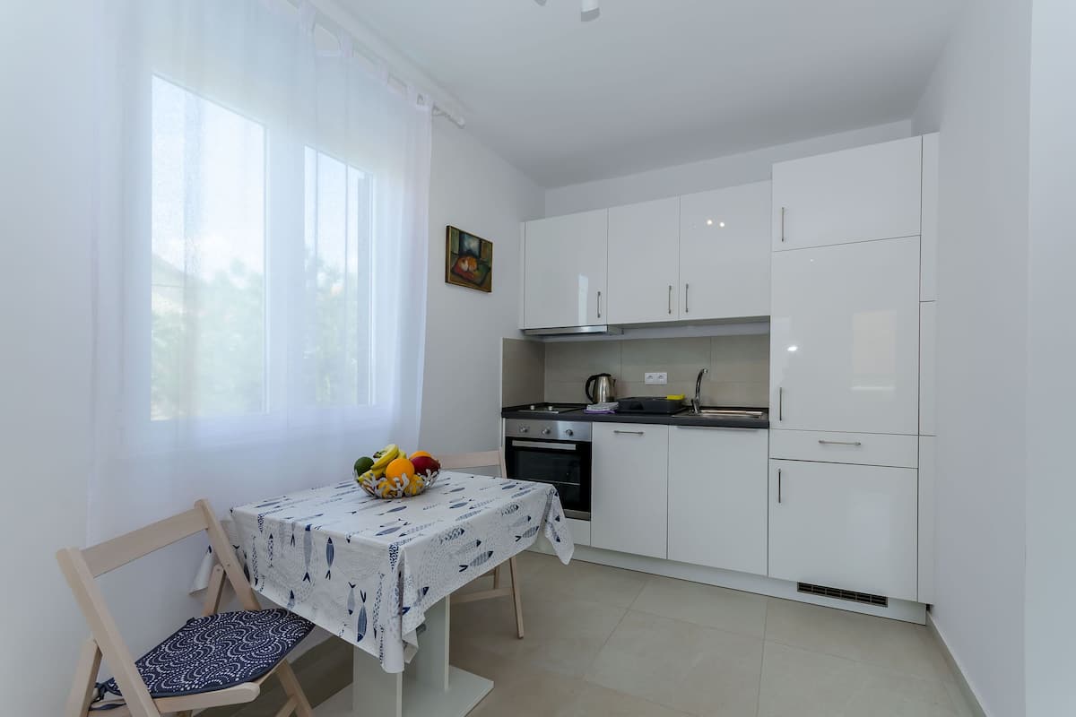 Une cuisine compacte avec des meubles blancs, une cuisinière à gaz et une petite table à manger accompagnée d’une chaise.