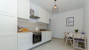 A modern kitchen with white cabinetry, a built-in oven, and a dining area with a wooden table and chairs. - Apartments Pleasures (Jelsa)