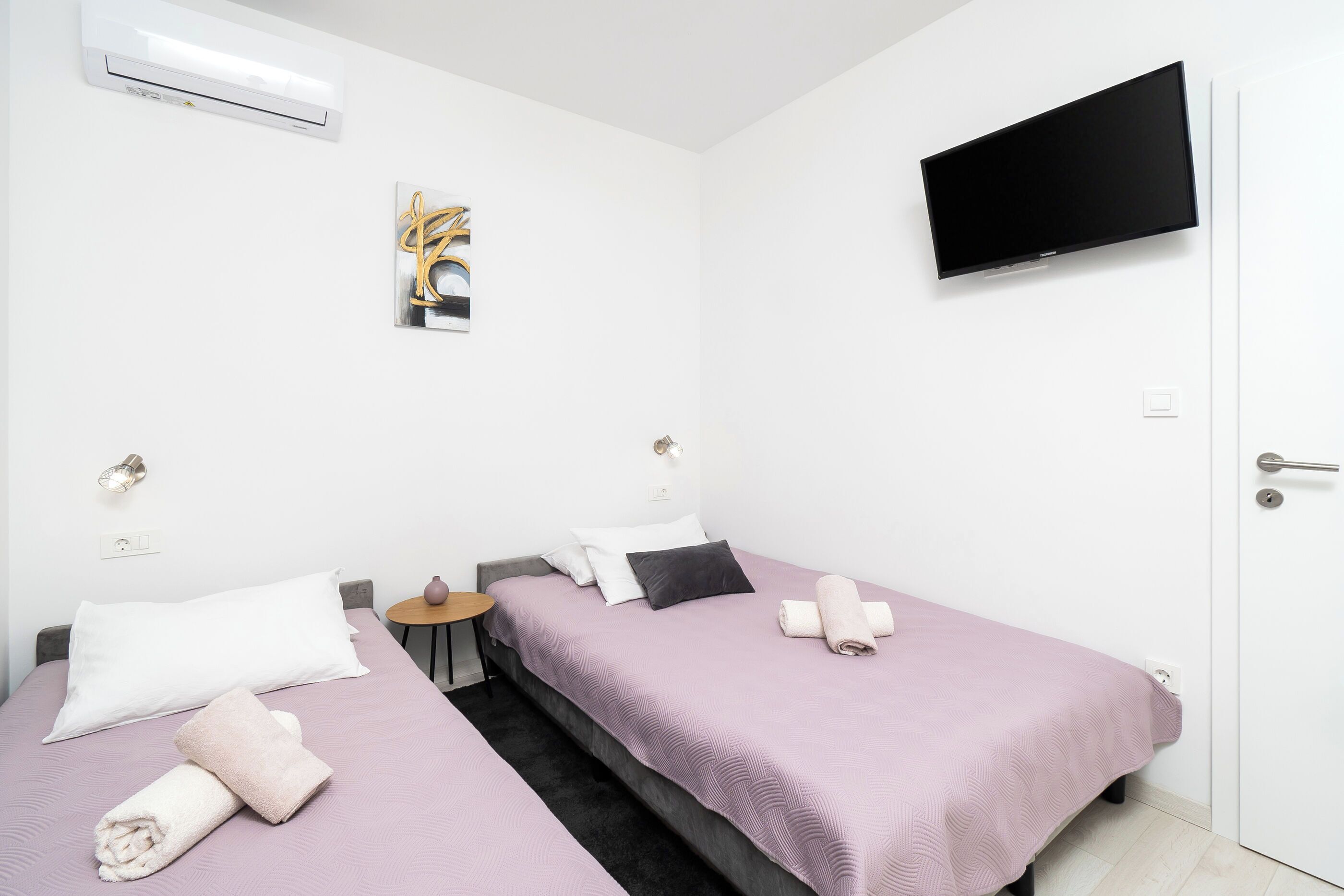 A hotel room with two beds, a TV mounted on the wall, and a small table.