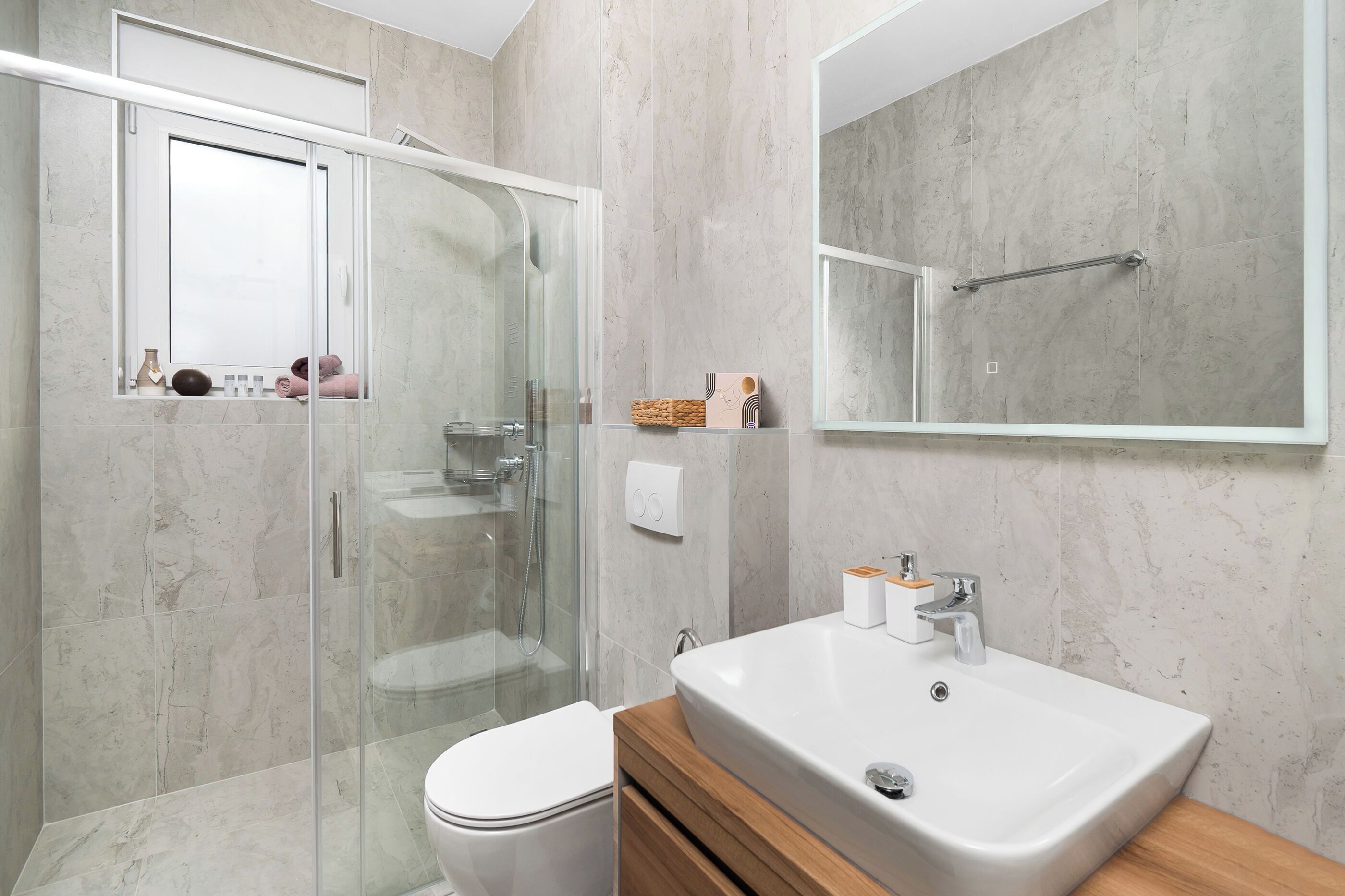 A modern bathroom with a glass-enclosed shower, a white toilet, and a large sink with a wooden vanity.