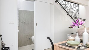 Une cuisine moderne avec une table à manger pour deux, un escalier avec une rampe en métal noir, et une vue sur la salle de bain adjacente.