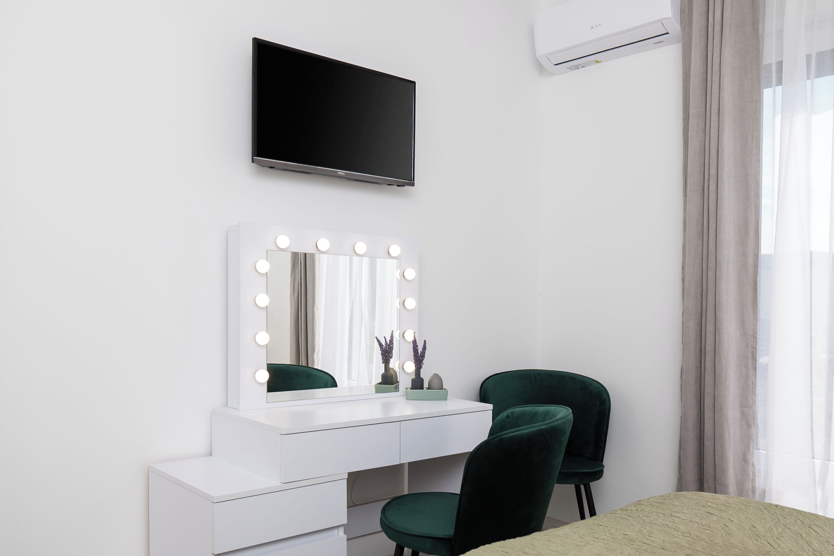 Una habitación moderna con tocador, sillas verdes, televisión de pantalla plana y aire acondicionado.
