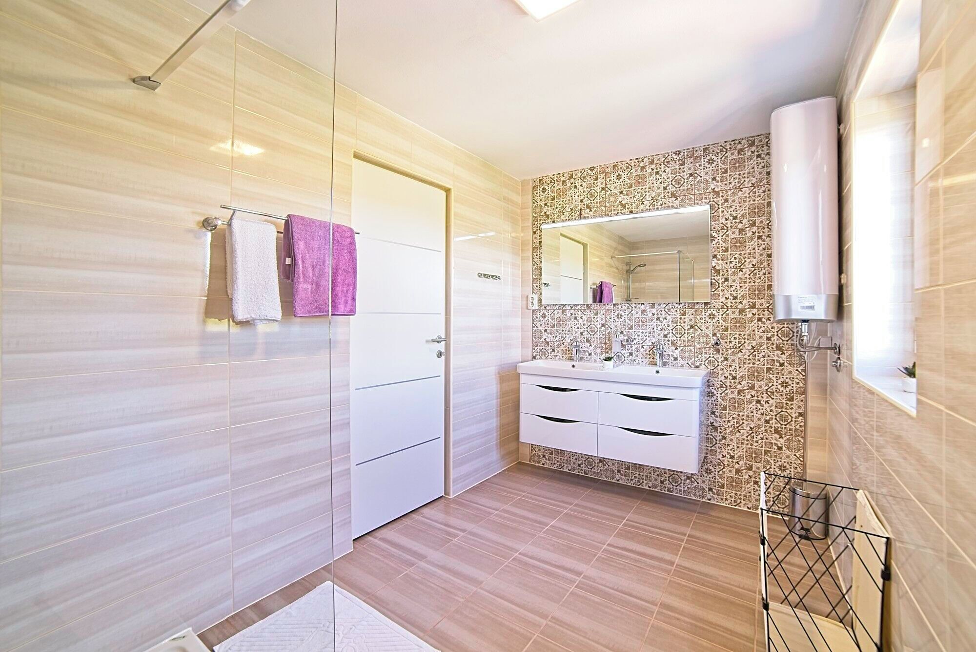 Een moderne badkamer met een inloopdouche, een wastafel met spiegel en een wand betegeld met patronen.