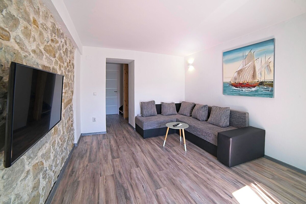 Een moderne woonkamer met een stenen muur, een grijze bank, een zwarte salontafel en een schilderij van een zeilboot.