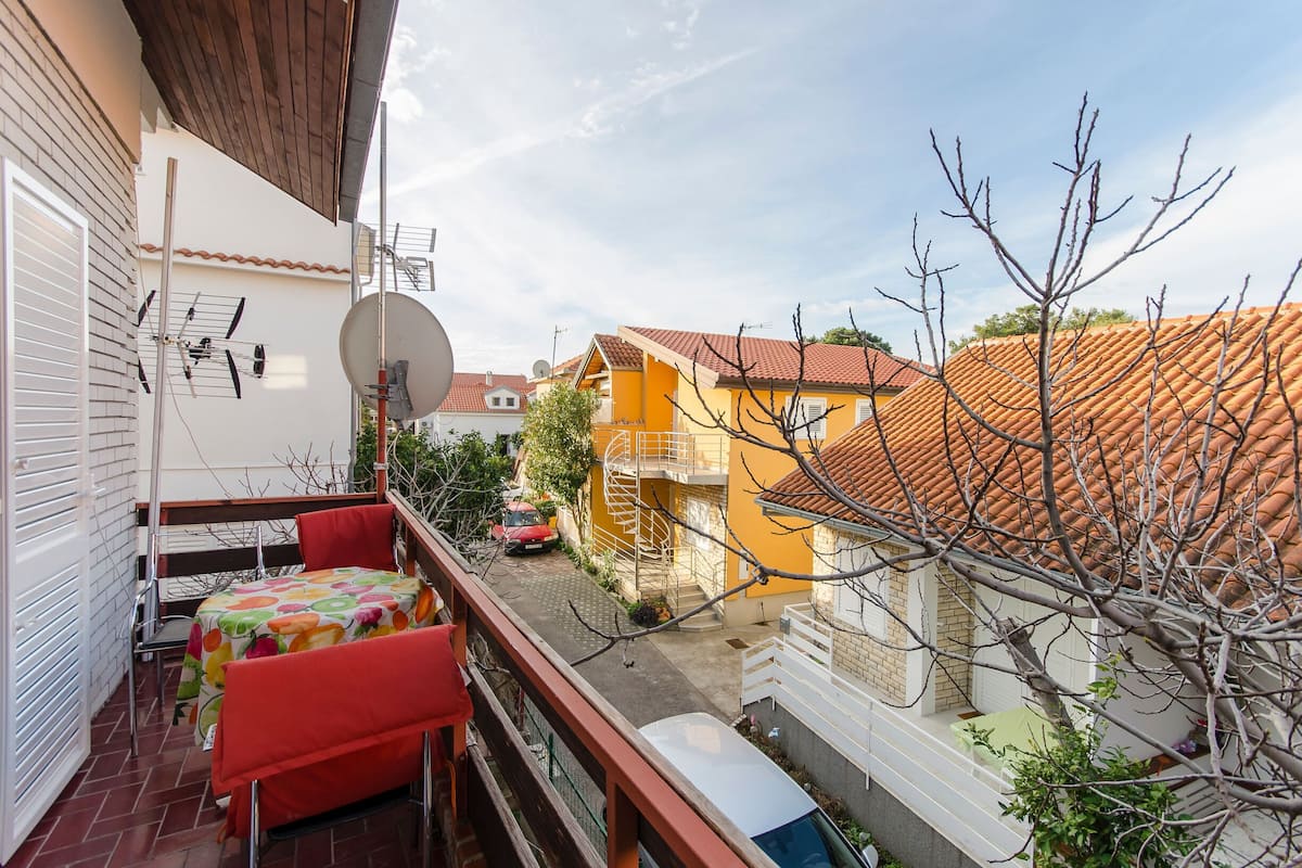 Ein Balkon mit Tisch und Stühlen, einer Satellitenschüssel und Blick auf die Nachbarhäuser.