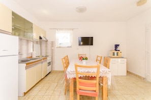 A compact kitchen with a dining table, chairs, a TV, and a microwave. - Apartments Dragica (Sibenik)