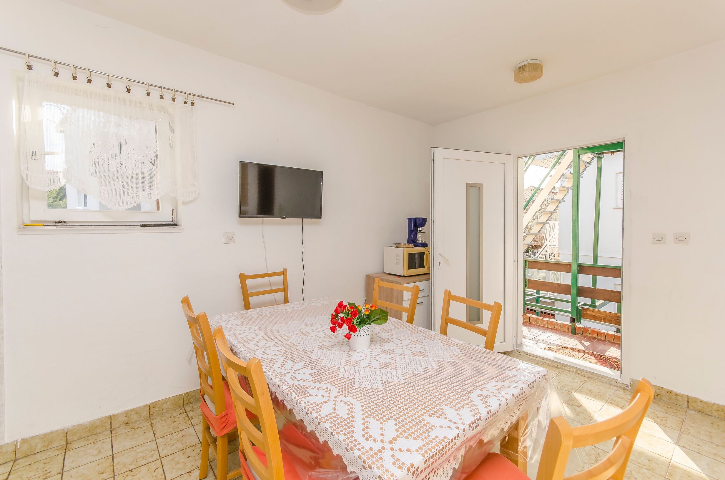 A dining area with a table, chairs, a TV, and a view of a staircase outside.