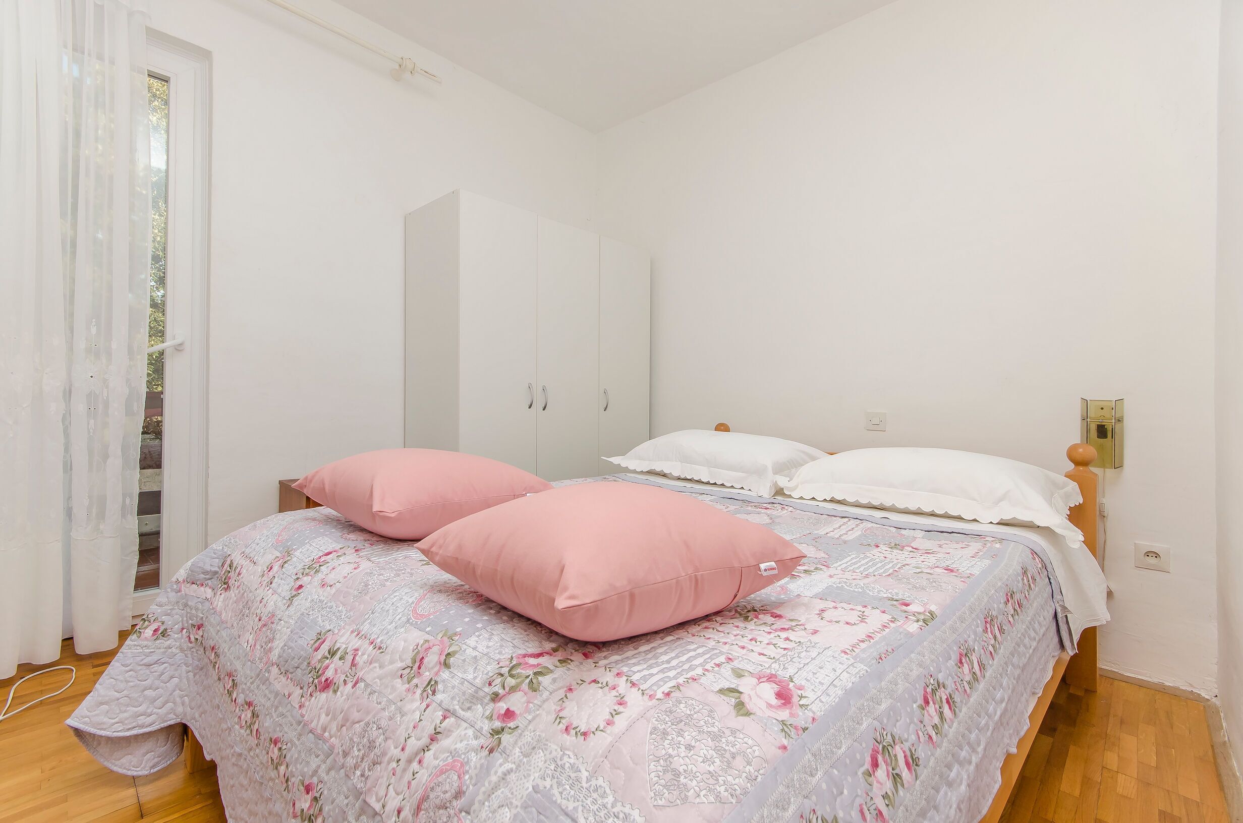 Et soveværelse med en seng, to pink og to hvide puder, en træsenggavl og en hvid garderobe.