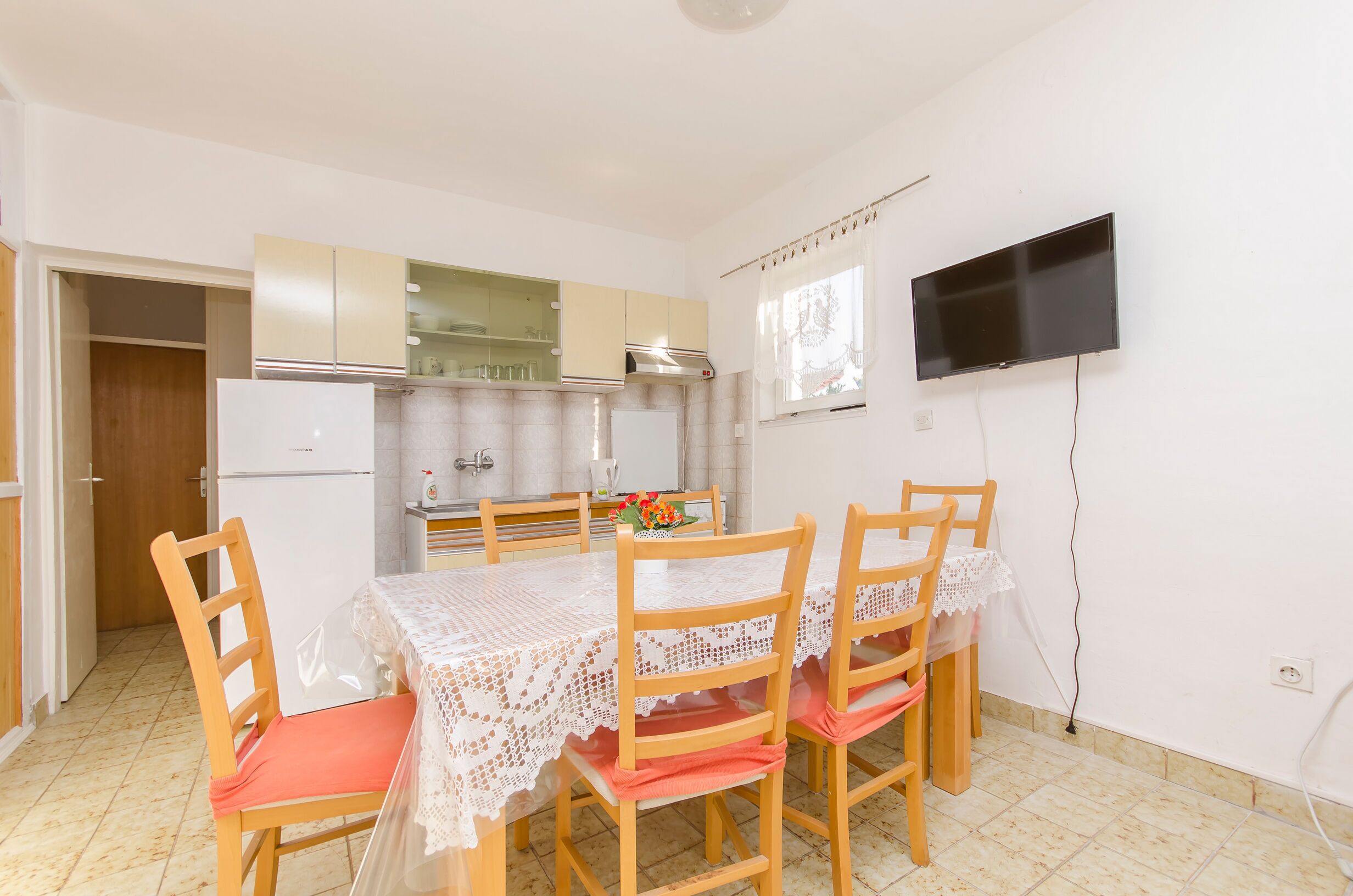 Un comedor con mesa y sillas, una cocina al fondo y un televisor montado en la pared.