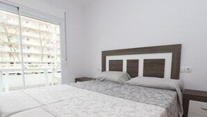 Et soveværelse med en stor seng, et natbord, en kommode og en skydedør, der fører til en balkon.