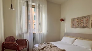 A bedroom with a bed, a chair, a window with sheer curtains, and a wall-mounted light fixture. - Botanical modernist home | Milanese living (Milano)
