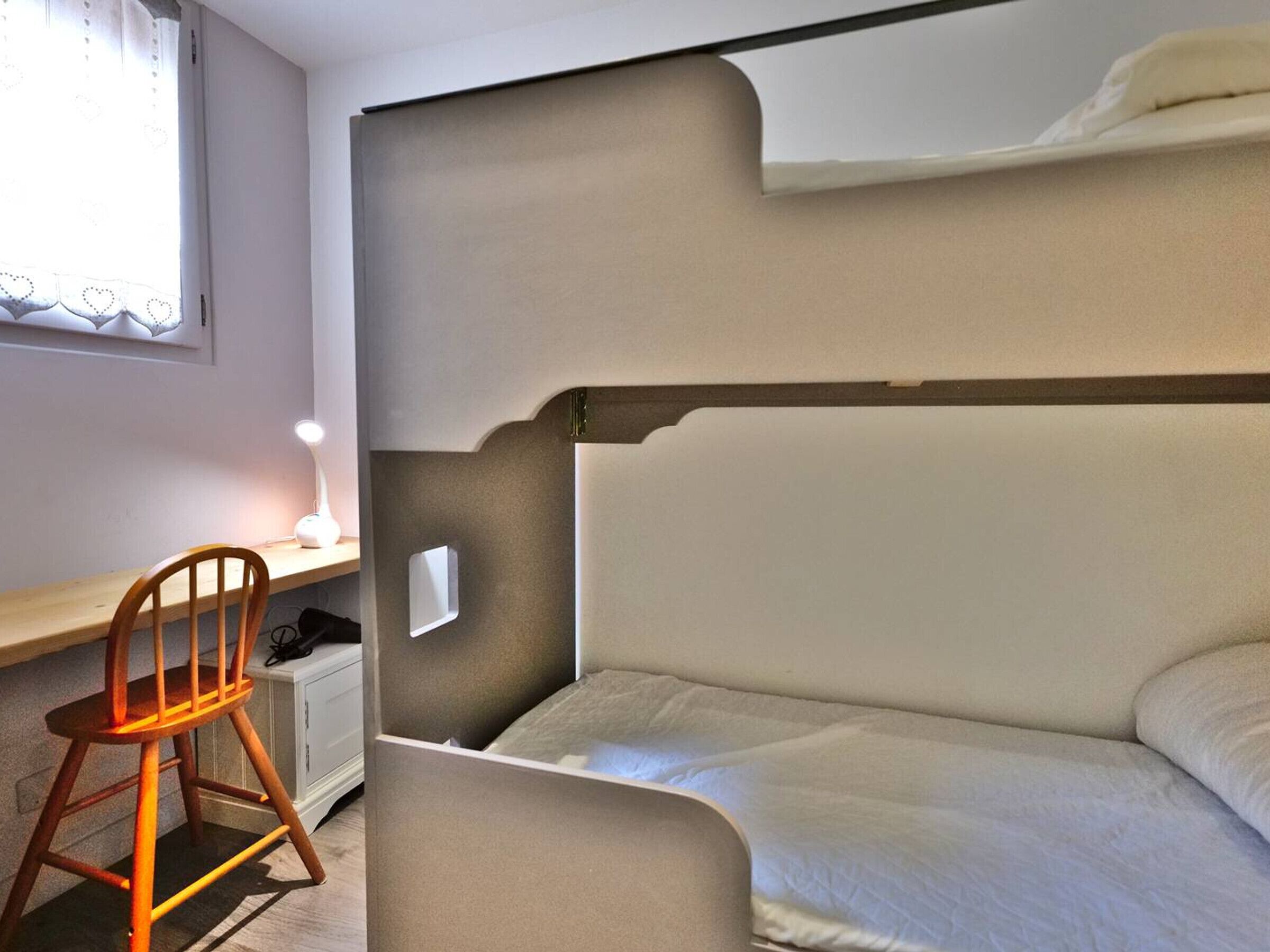 Ein Schlafzimmer mit einem Etagenbett, einem Schreibtisch mit Stuhl und einer Nachttischlampe.