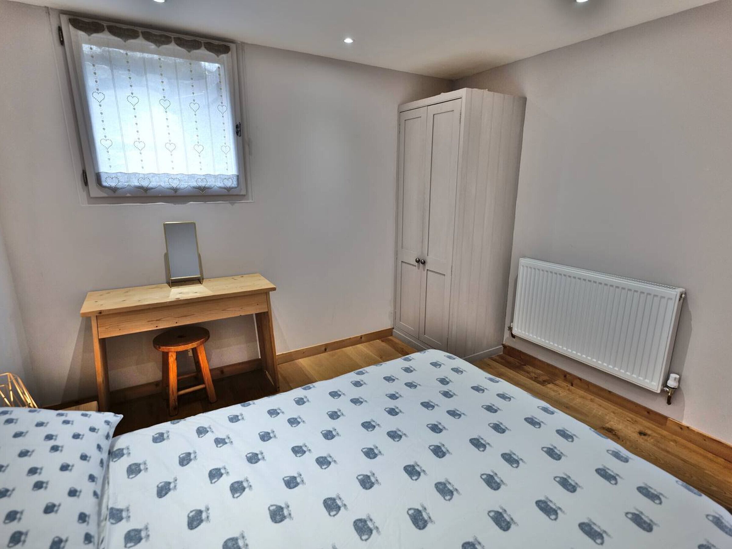 A bedroom with a bed, a desk, a wardrobe, and a radiator.