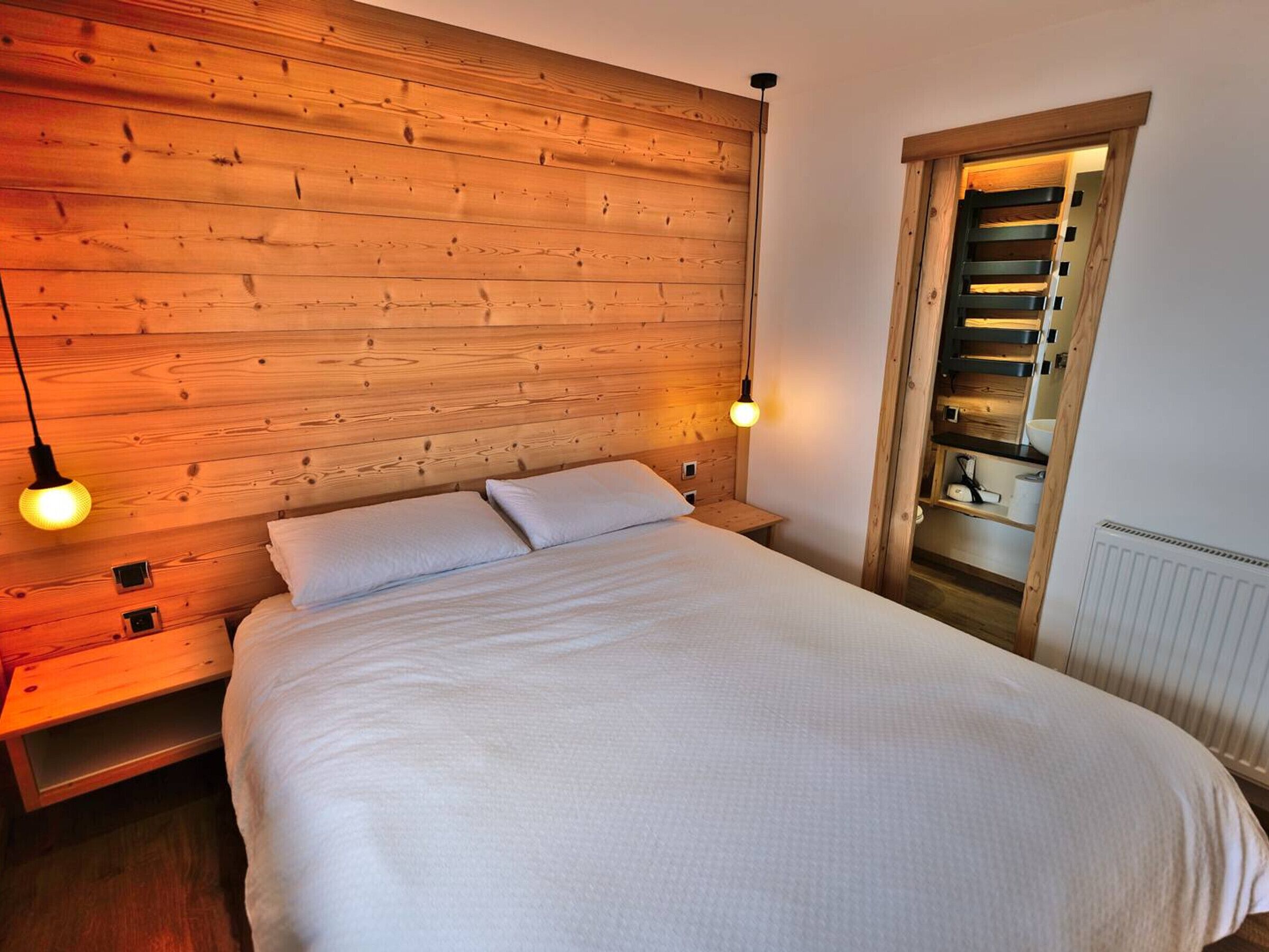 Un dormitorio con cabecera de madera, dos lámparas de noche, una cama con ropa de cama blanca y un armario empotrado con espejo.