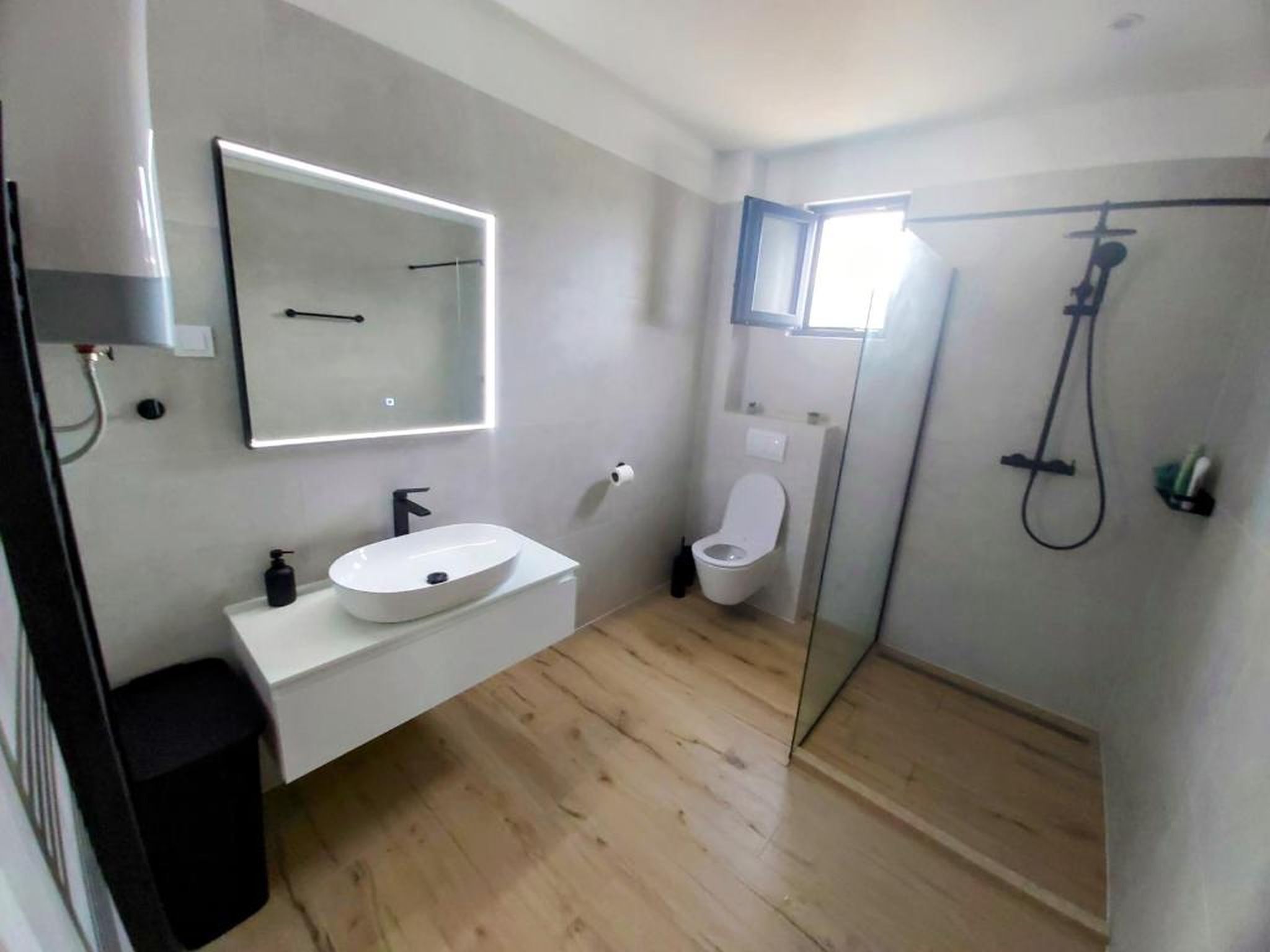 Een moderne badkamer met een wit wastafelmeubel, een grote spiegel, een toilet en een douchecabine met glazen wanden.