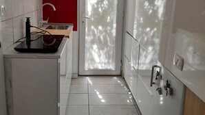 Moderni keittiö, jossa on valkoiset kaapit, punainen tehosteseinä, sisäänrakennettu liesi ja lasiovi, joka johtaa parvekkeelle.