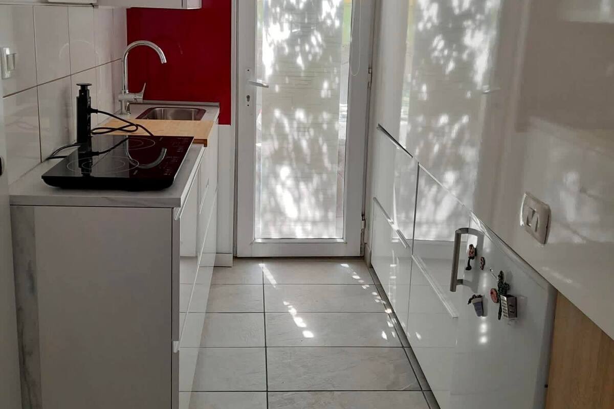 A modern kitchen with white cabinets, a red accent wall, a built-in stove, and a glass door leading to a balcony.