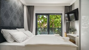 A hotel room with a large bed, a flat-screen TV, a window with a view of trees, and a patterned wall. - Villa Tria Quercus (Vodice)